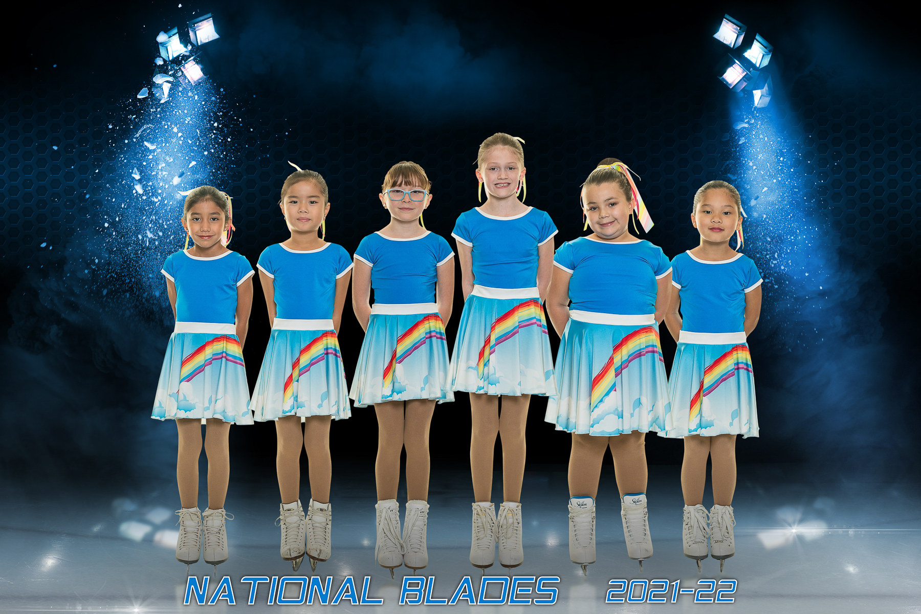 Six young girls in blue top and light blue with rainbow dress in figure skates.